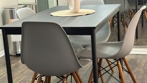 A modern dining area with a rectangular table, grey chairs with wooden legs, and a vase with pink flowers on a woven placemat. - Cozy 2-bedroom townhome by Galleria Houston with Pool & BBQ (Houston)