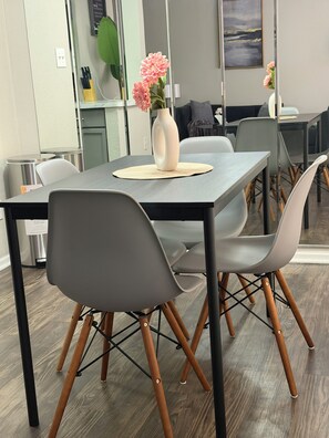 Ein stilvoller Essbereich mit einem rechteckigen Tisch, grauen Stühlen mit Holzbeinen und einer Vase mit rosa Blumen auf einer gewebten Tischunterlage.