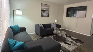A modern living room with a sectional sofa, a coffee table, and a flat-screen TV mounted on the wall. - Cozy 2-bedroom townhome by Galleria Houston with Pool & BBQ (Houston)