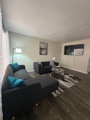 Ein modernes Wohnzimmer mit einem Ecksofa, einem Couchtisch und einem an der Wand befestigten Flachbildfernseher.