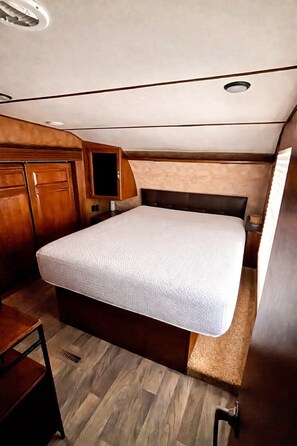 A compact RV interior with a bed, wooden cabinets, and a small seating area. - Trailer at the Peters Pond on beautiful Cape Cod! (Sandwich)