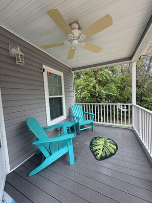 Une véranda avec deux fauteuils Adirondack turquoise, un ventilateur de plafond et une fenêtre sur laquelle on peut voir un panneau McDonald's.