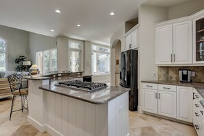 A spacious kitchen with white cabinetry, a central island with a stove, and a refrigerator. - 9 Beach Lagoon | Lagoon Luxury with Infinity Pool | Walk to the Beach (Hilton Head Island)