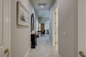 A hallway with a carpeted floor, a wooden cabinet, a mirror, and a door with a gold handle. - 9 Beach Lagoon | Lagoon Luxury with Infinity Pool | Walk to the Beach (Hilton Head Island)