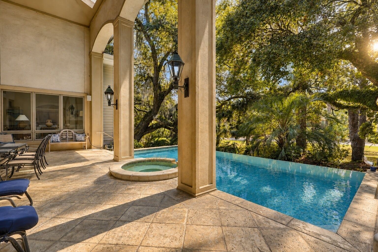 An outdoor swimming pool area with a hot tub, seating, and a view of trees.