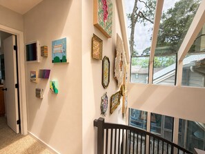 A hallway with a staircase leading to a balcony, decorated with various artworks and a view of the outside. - 82 South Sea Pines: Artful Midcentry Modern Living in the Heart of Sea Pines (Hilton Head Island)