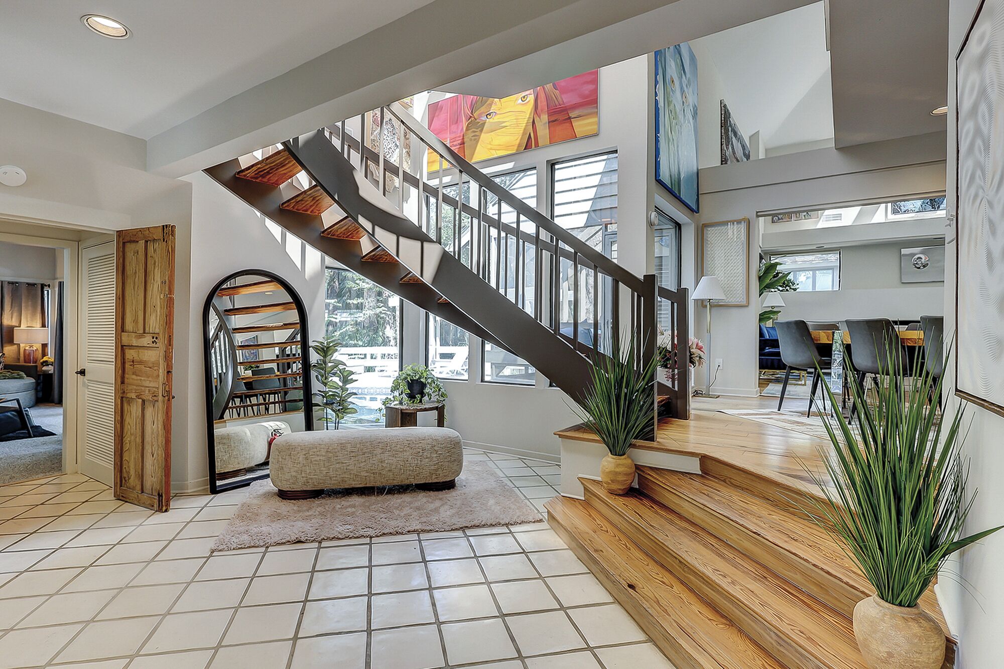 A spacious living area with a wooden staircase, a large window, and a view of the outdoors.