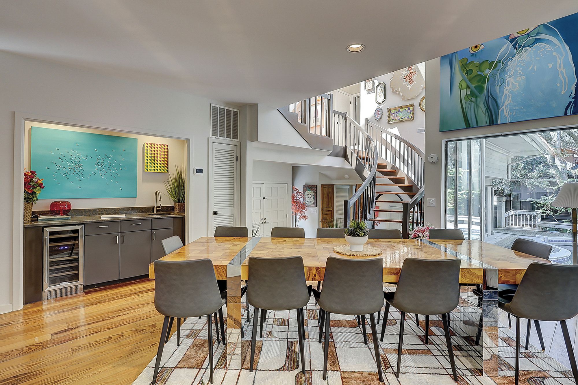 A modern dining area with a wooden table and chairs, a staircase, and a large window.