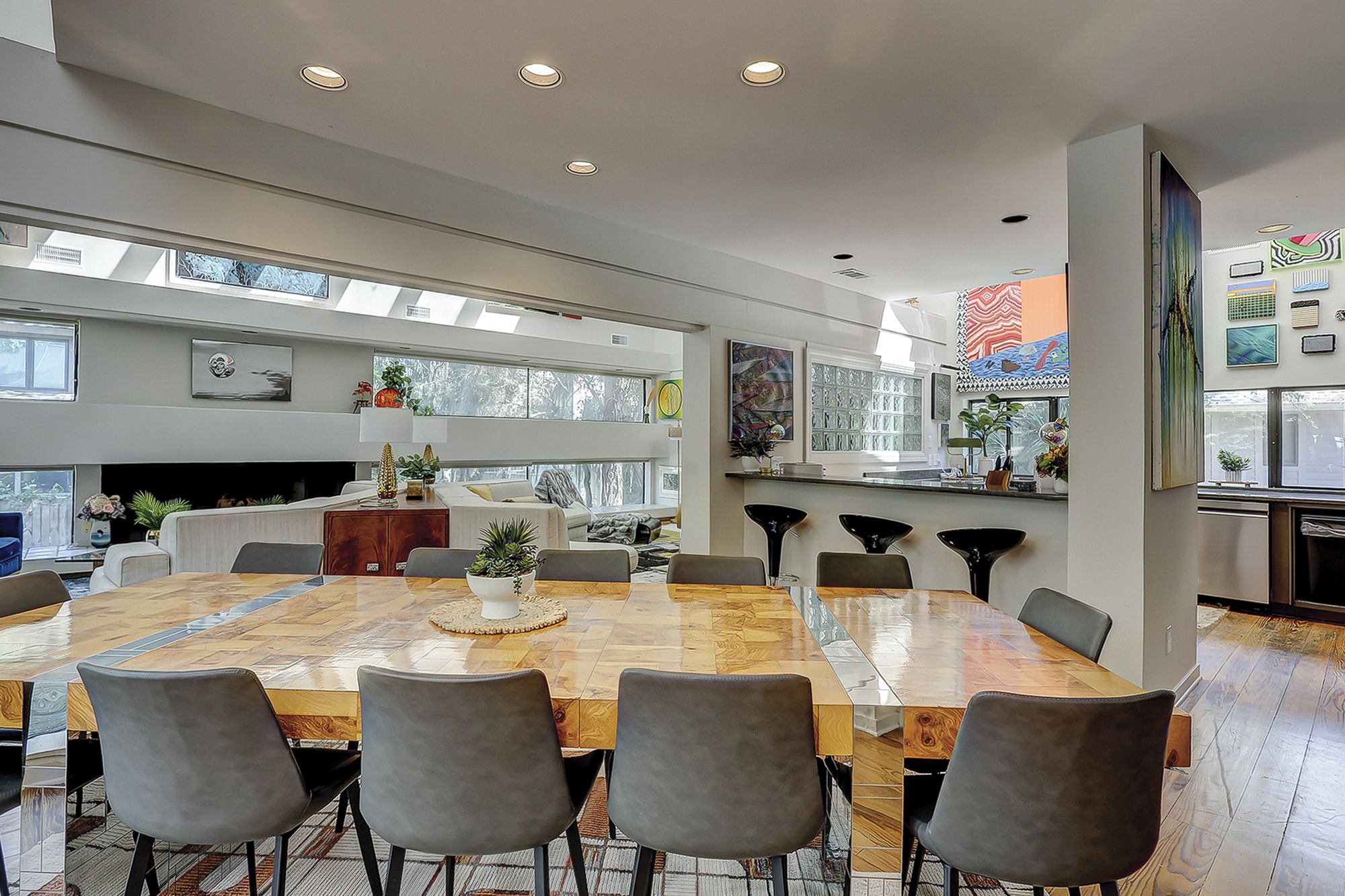 A spacious dining area with a large wooden table surrounded by chairs, a kitchen area with modern appliances, and a living space with a fireplace and large windows.