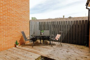 A patio with a table and chairs, a potted plant, and a wooden deck.
