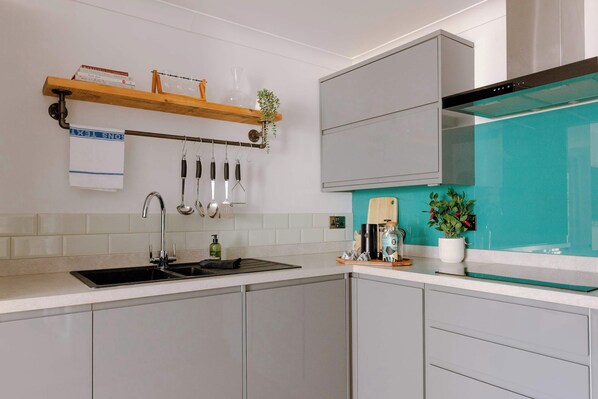 A modern kitchen with a stainless steel sink, a range hood, and a teal backsplash.