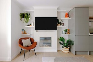 A modern living room with a flat-screen TV mounted above a fireplace, surrounded by shelves with decorative items and plants.