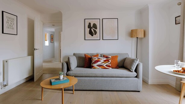Ein modernes Wohnzimmer mit einem grauen Sofa, einem kleinen runden Tisch und einer Stehlampe.