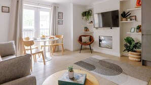 Ein modernes Wohnzimmer mit Essbereich, einem an der Wand montierten Flachbildfernseher sowie diversen Pflanzen und Dekorationselementen.