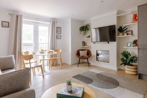 A modern living room with a dining area, a flat-screen TV mounted on the wall, and a variety of plants and decorations. - The Travelers Rest - Central Frome (Somerset)