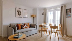 Ein modernes Wohnzimmer mit einem grauen Sofa, einem kleinen runden Tisch und einem Essbereich mit einem weißen Tisch und Holzstühlen.