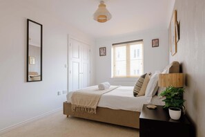 A bedroom with a bed, a bedside table, a lamp, a window with blinds, and a door. - The Travelers Rest - Central Frome (Somerset)