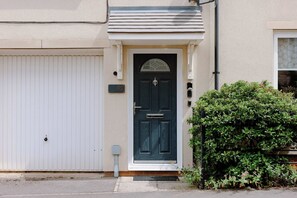 A residential building with a dark blue front door, a white garage door, and a small garden with green shrubs. - The Travelers Rest - Central Frome (Somerset)