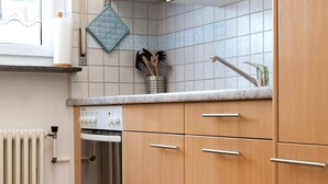 Una cucina con mobili in legno, forno integrato, bollitore e schienale piastrellato.