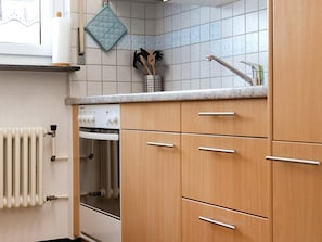 Eine Küche mit Holzausstattung, einem Einbauofen, einem Wasserkocher und einer gefliesten Spritzschutzwand.