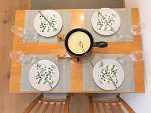 Ein Esstisch mit vier Tellern, auf jedem ein Messer und eine Gabel, sowie eine zentrale Schüssel mit Essen.