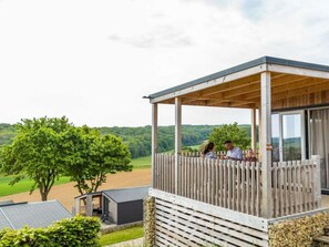 A covered outdoor area with a wooden deck, a stone wall, and a view of a green landscape.