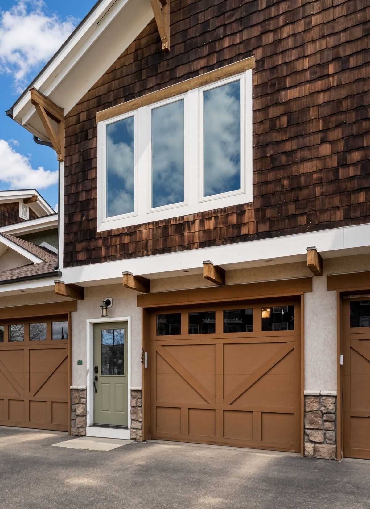 A two-story house with a brown shingle exterior, a front door, and two garage doors.