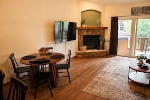 Una sala de estar con chimenea, una mesa de comedor con sillas, un televisor de pantalla plana montado en la pared y vistas a través de un ventanal.