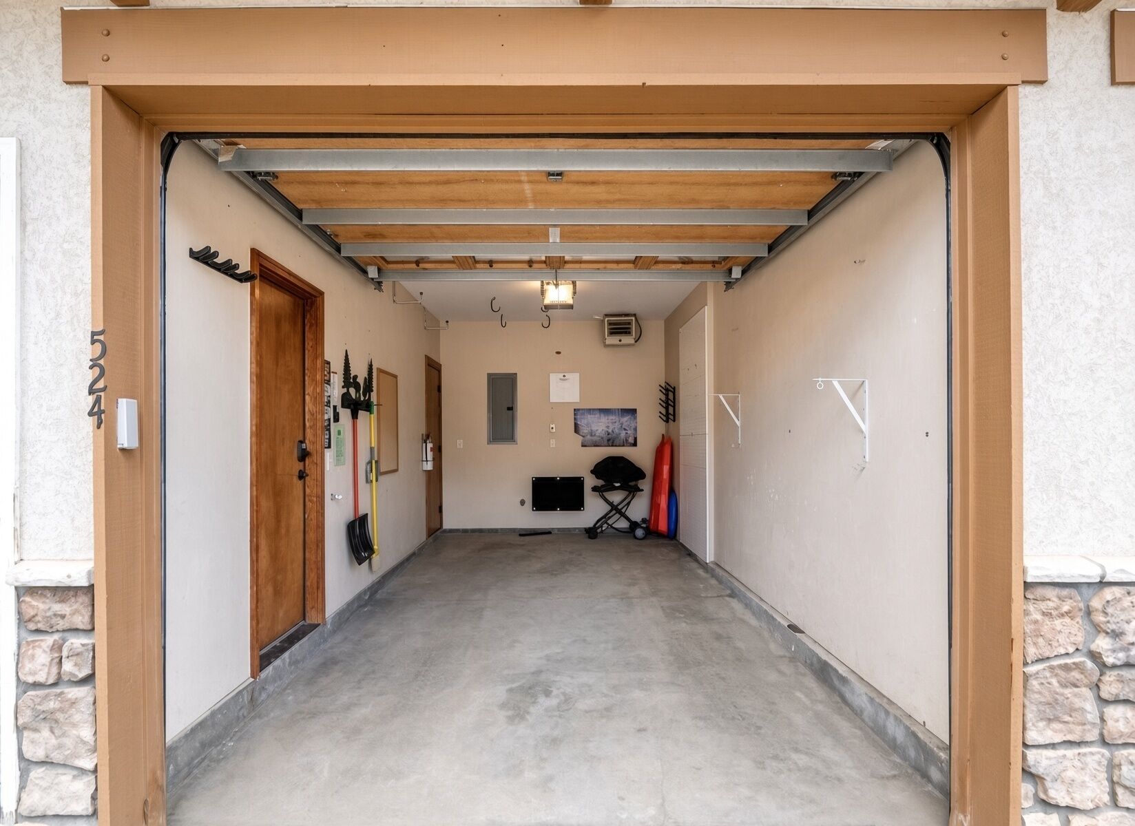 Een garage met een betonnen vloer, een houten deur en een metalen dakconstructie.