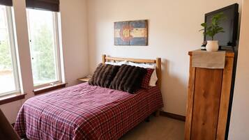 A bedroom with a bed, a nightstand, a painting, a television, and a window.