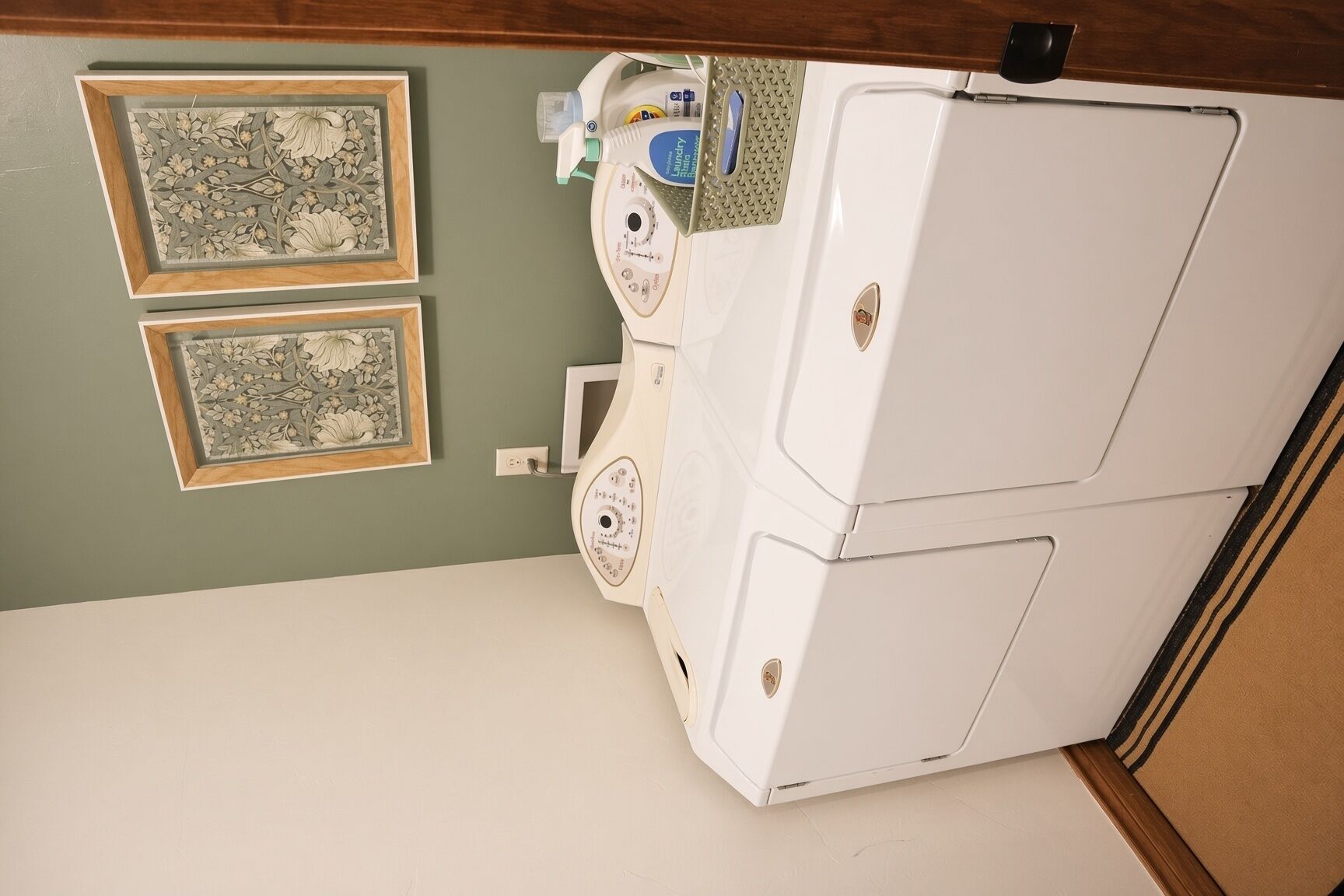 A laundry area with a washing machine, two framed floral wall decorations, and a laundry basket on the counter.