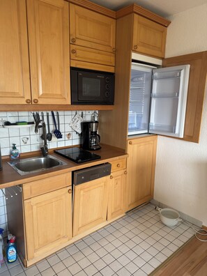 A compact kitchen with wooden cabinets, a built-in microwave, a coffee maker, and a dishwasher. - Heimathafen Harz Vacation Rental – Hohegeiß, Pool & Sauna (Braunlage)