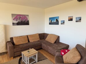 A living room with a brown sectional sofa, a small wooden side table, and a red throw pillow. - Heimathafen Harz Vacation Rental – Hohegeiß, Pool & Sauna (Braunlage)
