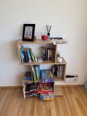 Ein Bücherregal mit verschiedenen Büchern, einem gerahmten Zertifikat, einem Glas mit einer roten Kerze und einer Fernbedienung.