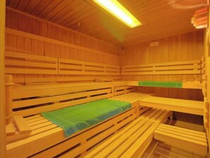 Ein Saunaraum mit Holzbänken und Bänken mit grünen Liegen.