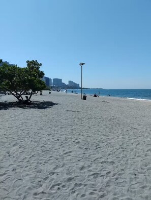 Une plage avec un arbre, un lampadaire et des bâtiments en arrière-plan.