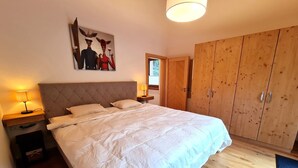 A bedroom with a large bed, wooden wardrobe, and a painting on the wall.