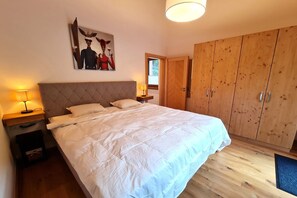 A bedroom with a large bed, wooden wardrobe, and a painting on the wall.