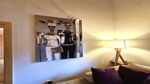 A room with a large painting of deer figures, a lamp, and a sofa with cushions.