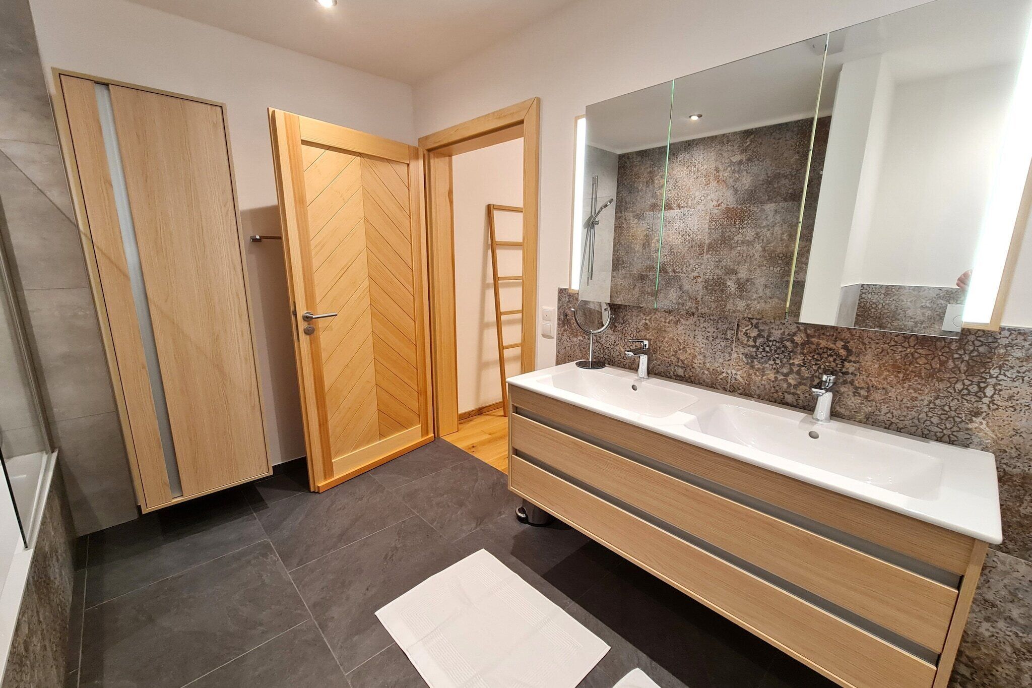 Een moderne badkamer met twee wasbakken, een grote spiegel en een houten wastafelmeubel.