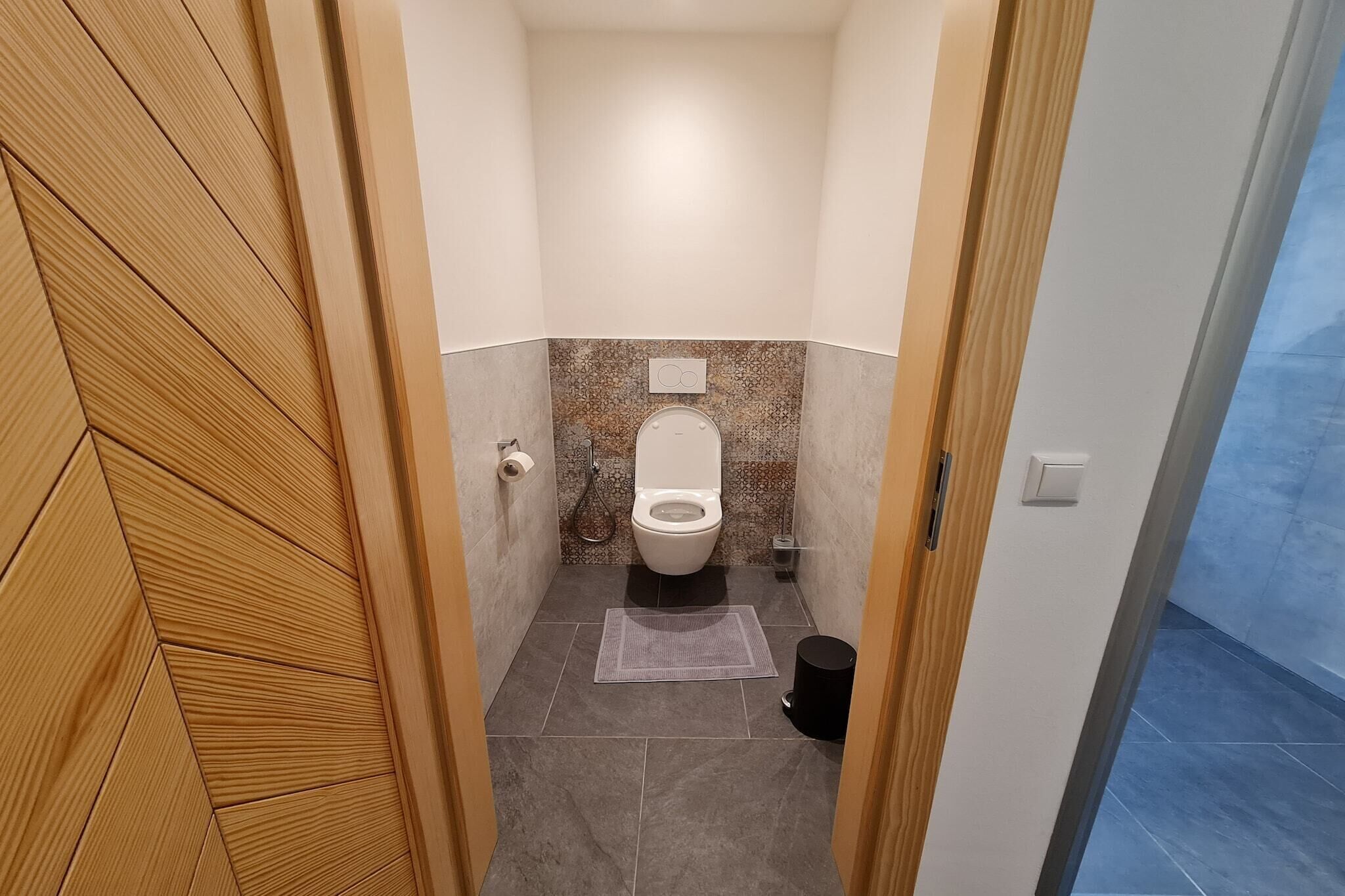 A small, narrow bathroom with a toilet, a shower, and a wooden door.
