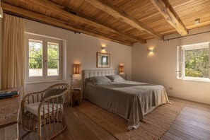 A bedroom with a large bed, two bedside lamps, a window with curtains, a wooden ceiling, and a wicker chair. - Villa with Pool near Motovun in Istrian Village (Prašćari)