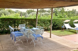 Eine Terrasse im Freien mit Tisch und Stühlen, einem überdachten Bereich und Blick auf einen Garten.