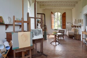 Ein Zimmer mit Holzboden, einem Esstisch mit Stühlen, einem Gemälde auf einem Staffelei und einem Fenster mit Rollläden.