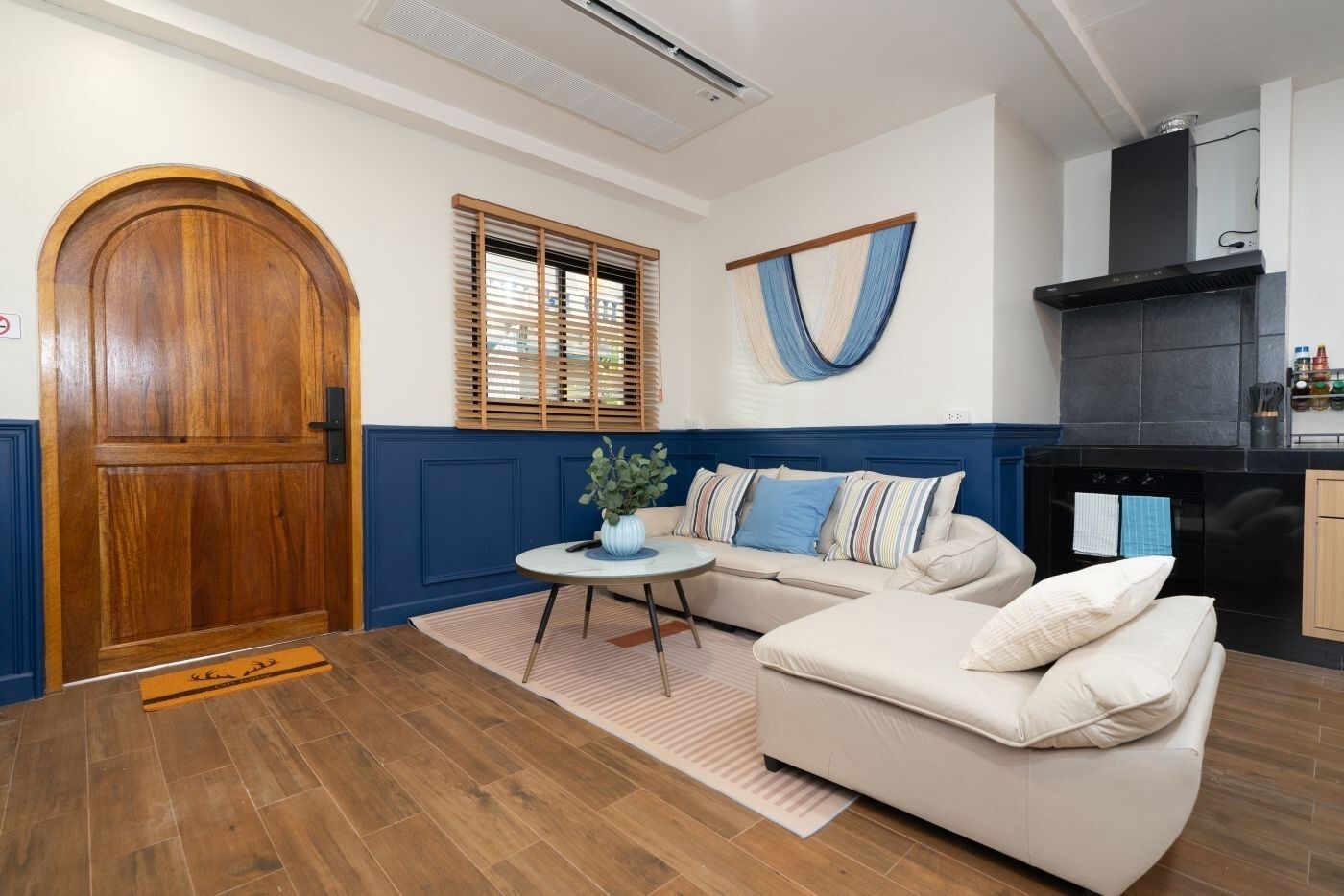 Una habitación con puerta de madera, pared azul decorativa, un sofá, una mesita redonda y una zona de cocina con estufa negra.