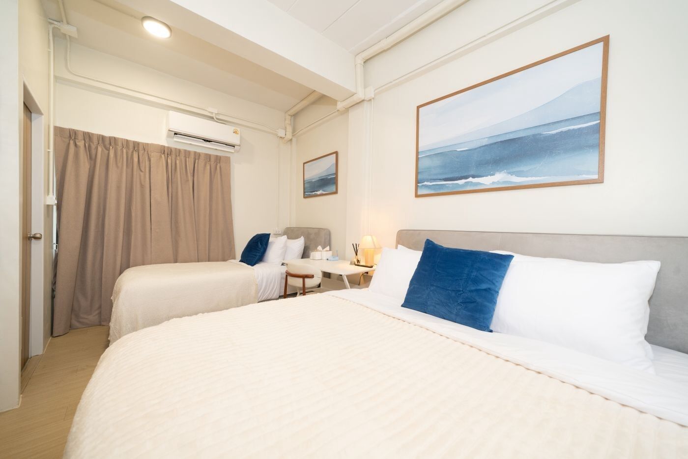 A hotel room with two beds, a desk, a chair, and an air conditioning unit.