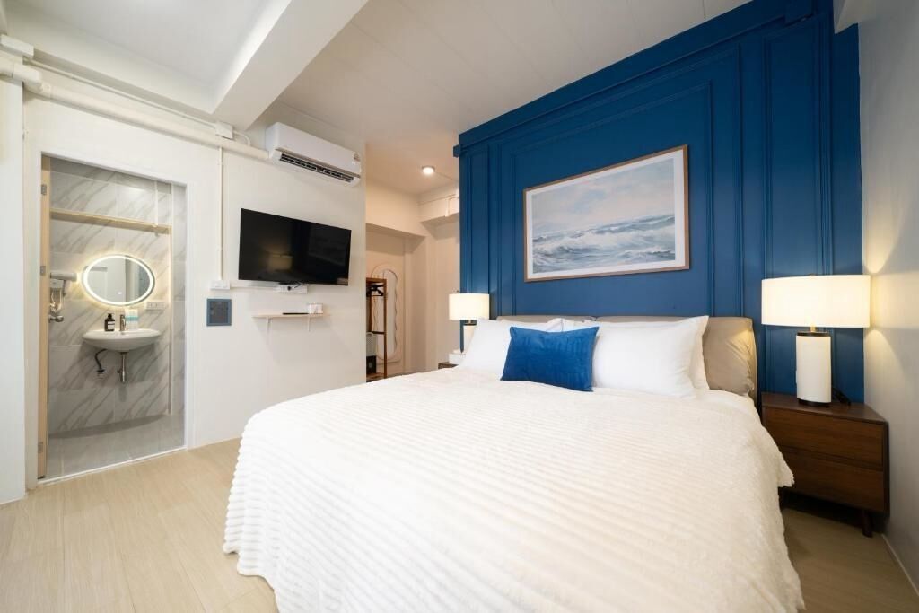 A hotel room with a large bed, a television, a painting on the wall, and a bathroom with a mirror and sink.