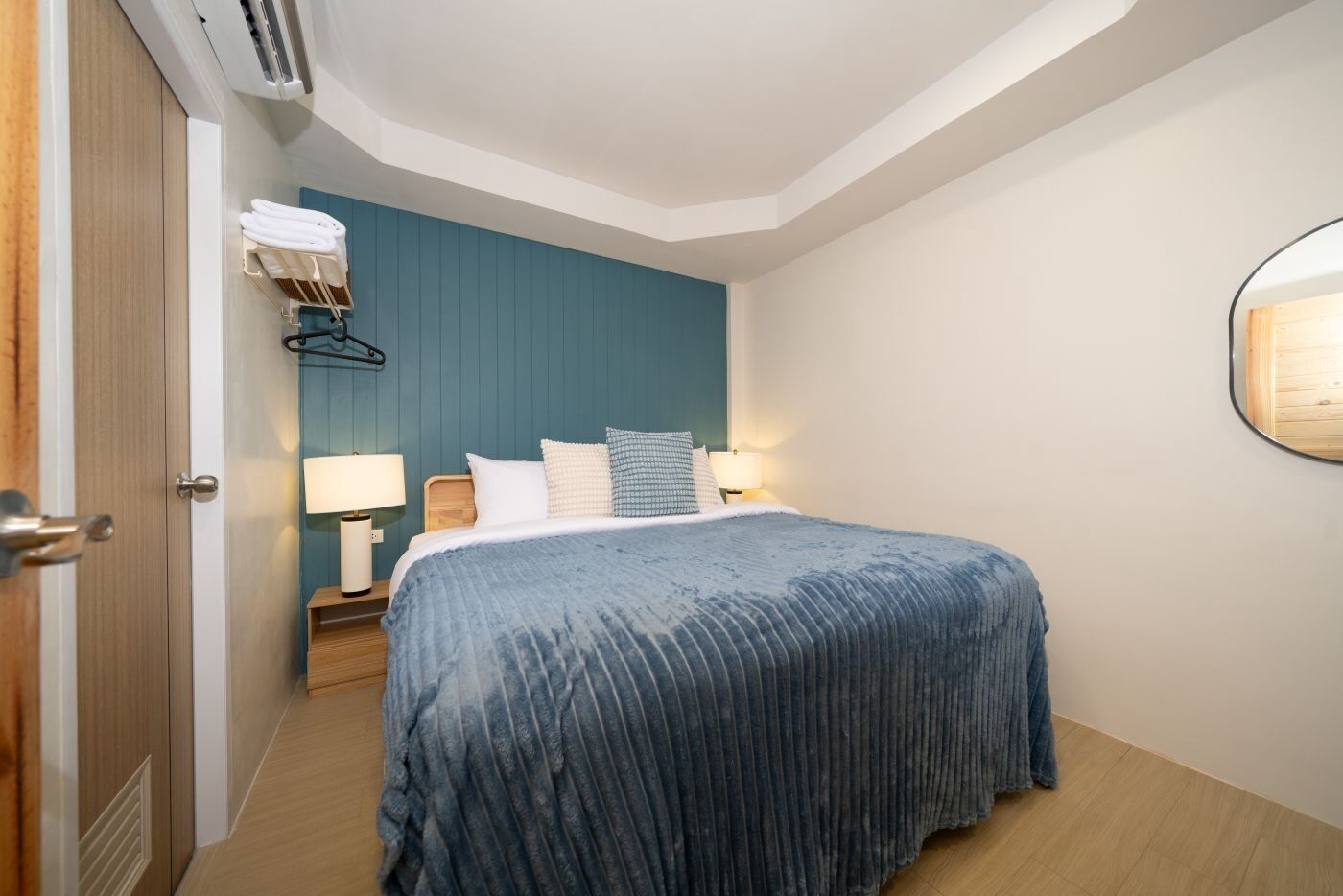 A hotel room with a bed, bedside lamps, a wall-mounted air conditioner, and a door.