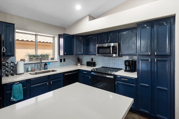 A modern kitchen with dark blue cabinets, a white countertop, a stainless steel microwave, and a black stove.