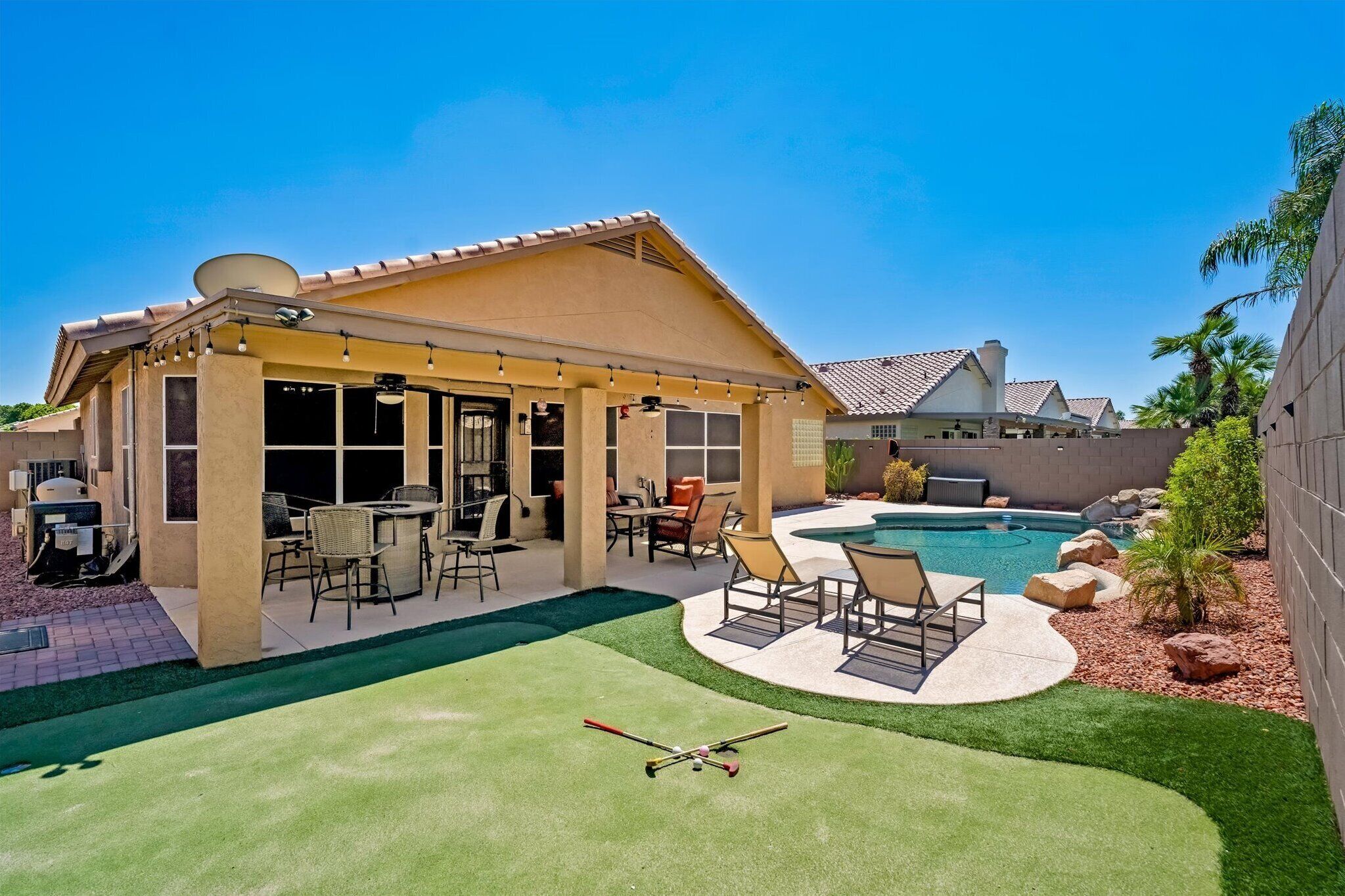 The backyard is designed for Arizona days — private pool, putting green, loungers, and shaded patio space.